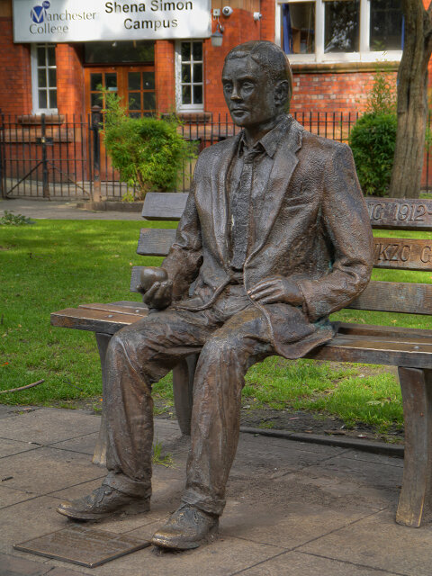 A estátua de Turing no Sackville Park, em Manchester, inaugurada em 2001. Ele está sentado num banco, segurando uma maçã.